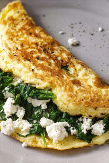 An spinach and feta omelet with spinach and crumbled feta cheese, cooked and folded in a non-stick pan.