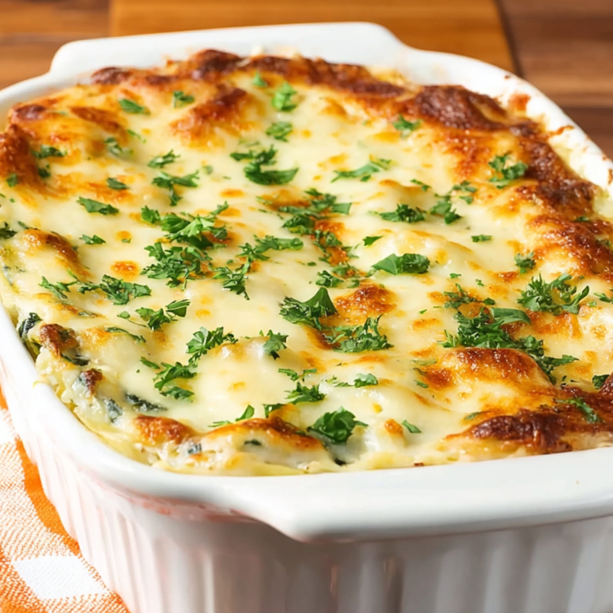 Uncooked spinach and mushroom lasagna in a white rectangular baking dish, layered with mushrooms, spinach, and shredded cheese, ready to bake, placed on a wooden surface.
