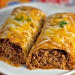 Two beef and cheese chimichangas on a white plate, topped with melted cheddar and mozzarella cheese, with the filling slightly visible at the ends, on a colorful floral background.