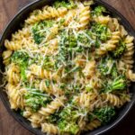Cooked Broccoli Cheese Pasta fusilli pasta in a black skillet, mixed with melted cheese, garnished with grated Parmesan and chopped herbs, creamy and cheesy texture, top-down view, ready to serve as a comfort food dish.