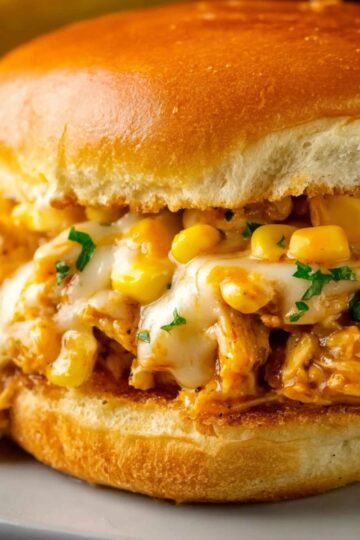 Close-up of a Cajun Chicken Sloppy Joes on a golden hamburger bun, filled with creamy cheesy chicken, corn, and garnished with chopped parsley.