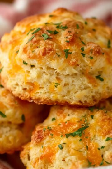 Close-up of fluffy Cheddar Bay Biscuits stacked together, showing a soft, airy interior with melted cheese and a sprinkle of chopped herbs on top.