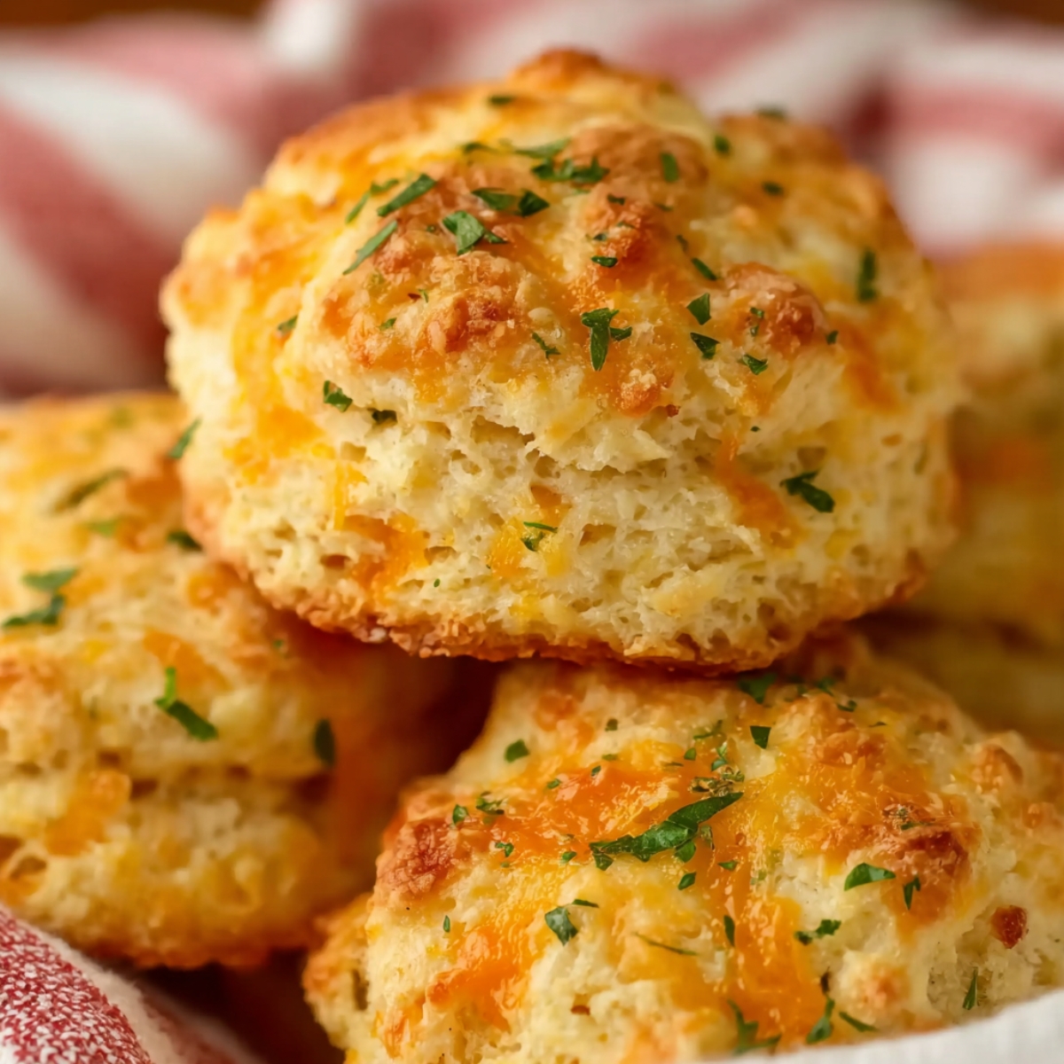 Close-up of fluffy Cheddar Bay Biscuits stacked together, showing a soft, airy interior with melted cheese and a sprinkle of chopped herbs on top.
