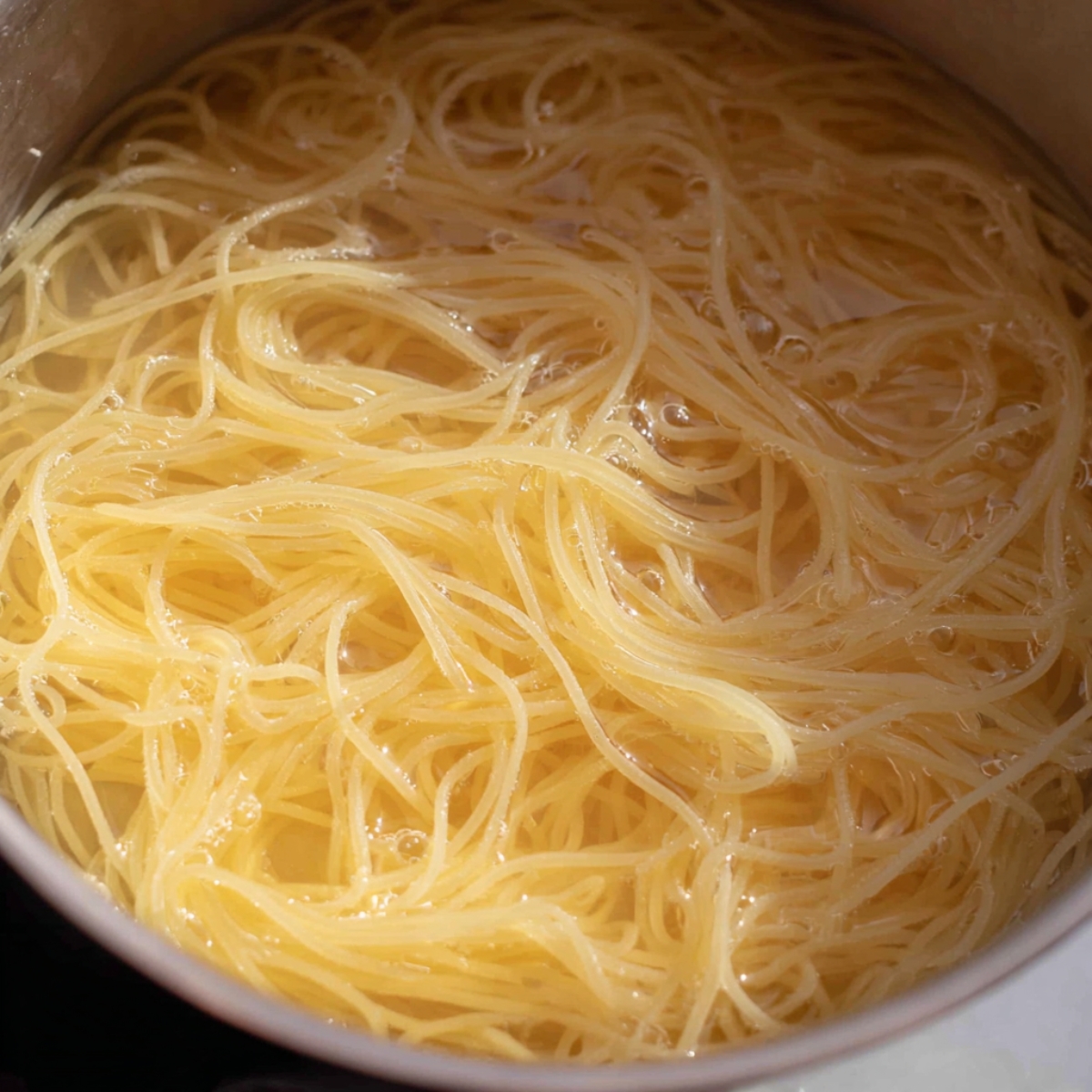 Close-up of thin spaghetti noodles cooking in a pot of boiling water, showing the strands fully submerged and gently swirling.