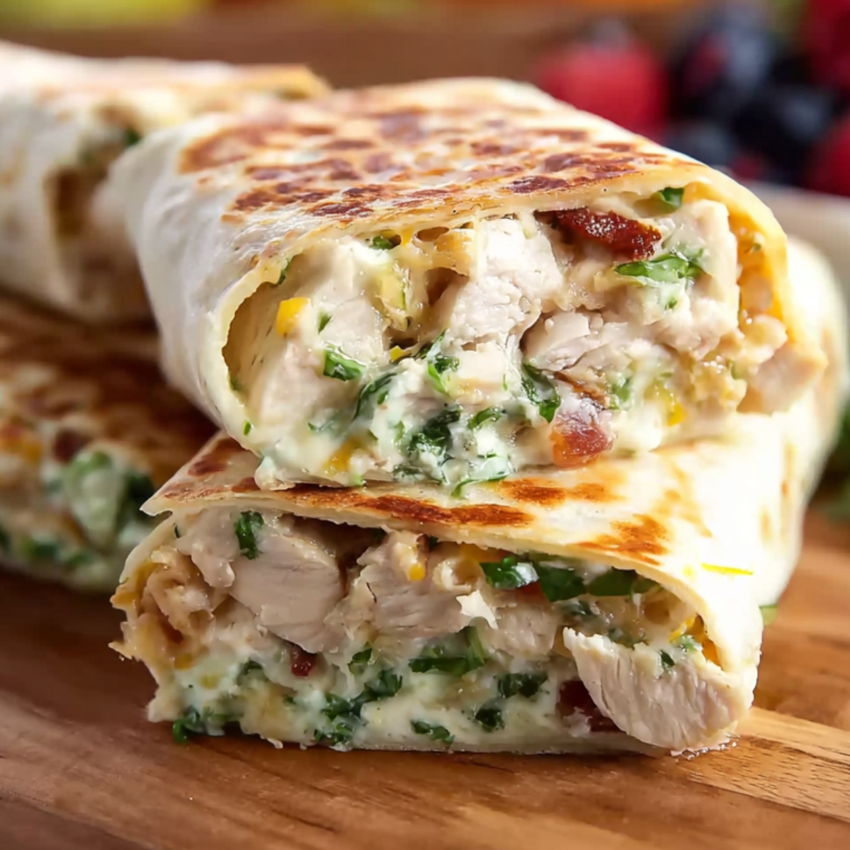 Close-up of Crispy Chicken Bacon Ranch Wraps cut in half, showing creamy filling with chicken, bacon, cheese, and fresh greens, stacked on a wooden board, appetizing and detailed.