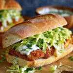 Crispy Chicken Caesar Sandwich on a crusty roll topped with shredded lettuce and creamy sauce, served on parchment paper with another sandwich blurred in the background.
