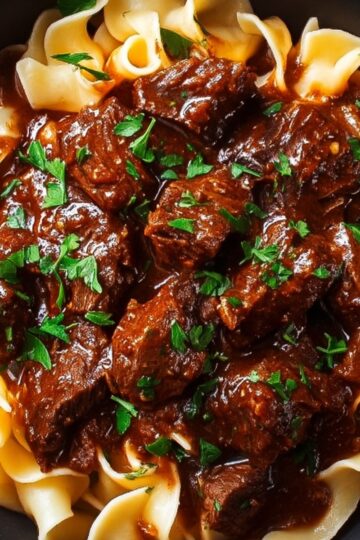 A close-up of a bowl of Korean Beef Noodles. Tender beef chunks in a dark, savory sauce sit atop egg noodles, garnished with fresh chopped herbs, creating a rich and appetizing presentation.