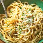 A bowl of Midnight Pasta Recipe tossed with melted butter, grated Parmesan cheese, and chopped parsley, with a fork twirling some noodles in a green bowl.