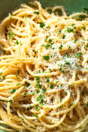A bowl of Midnight Pasta Recipe tossed with melted butter, grated Parmesan cheese, and chopped parsley, with a fork twirling some noodles in a green bowl.