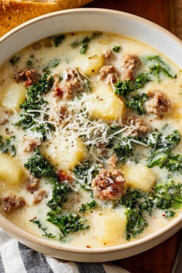 Bowl of Olive Garden Zuppa Toscana Soup, kale, and potatoes topped with grated cheese, served with bread on the side.