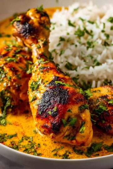 Grilled Paprika Chicken Drumsticks coated in creamy orange paprika sauce, served with fluffy white rice in a white bowl, garnished with fresh chopped cilantro, close-up, appetizing presentation.