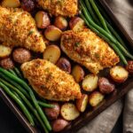 Close-up of a Parmesan Crusted Chicken Sheet Pan Dinner with baked parmesan-crusted chicken breasts, roasted red potatoes, and steamed green beans, golden brown and garnished with fresh herbs.