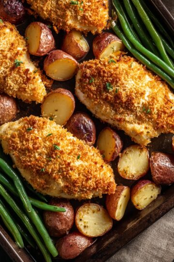 Close-up of a Parmesan Crusted Chicken Sheet Pan Dinner with baked parmesan-crusted chicken breasts, roasted red potatoes, and steamed green beans, golden brown and garnished with fresh herbs.