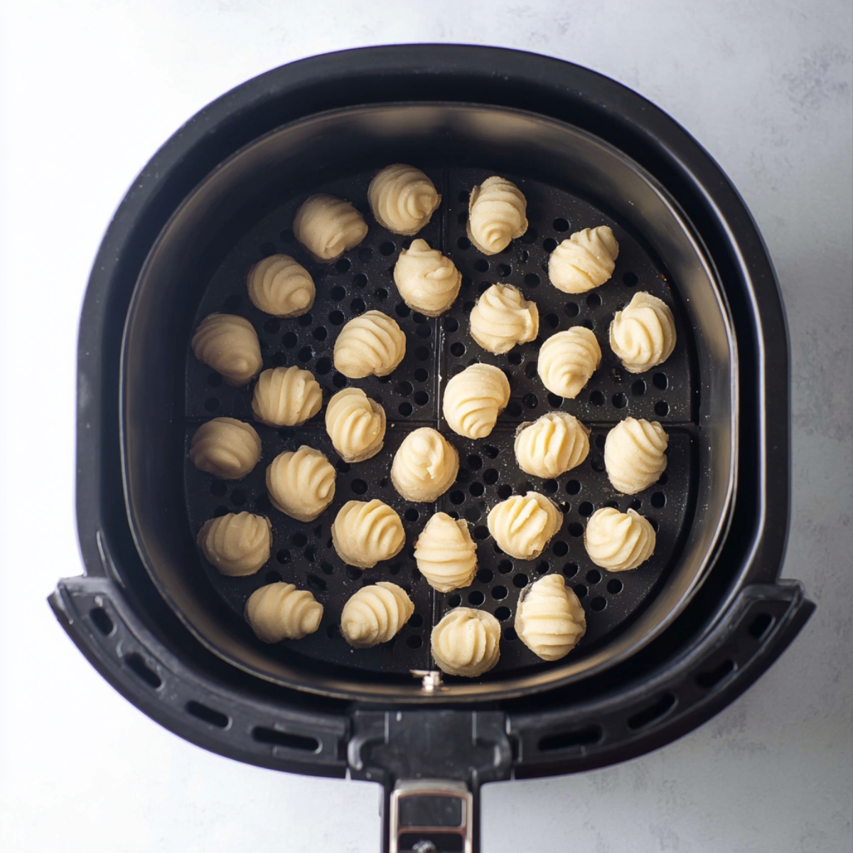Top-down view of an air fryer basket filled with piped churro dough bites, evenly spaced and ready to cook.