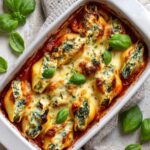Baked Ricotta and Spinach Stuffed Shells in a white rectangular dish, topped with melted cheese and garnished with fresh basil leaves, with a rustic textured background and a light-colored napkin.