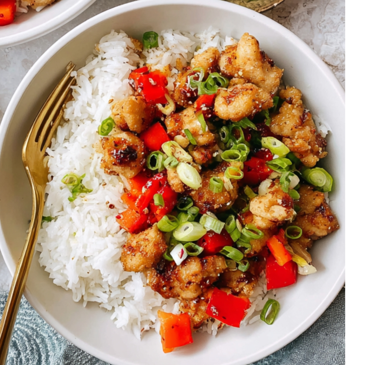 A bowl of cooked Salt And Pepper Chicken served over white rice, topped with diced red bell peppers and sliced green onions, gold fork in the bowl, overhead view, bright natural lighting, appetizing Asian-style meal.