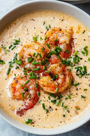 White bowl filled with creamy seafood bisque, topped with cooked shrimp, finely chopped chives, and a sprinkle of black pepper, overhead view, rich and smooth texture, appetizing presentation.